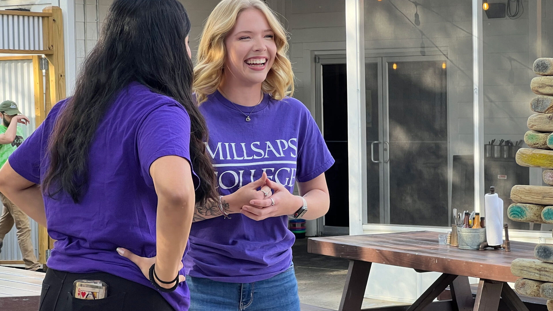 A blonde female student in her purple Millsaps tee shirt laughs with her friend as they play a game of giant Jenga outside.