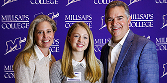 A student in a nametag poses with her parents in front of a Millsaps College step and repeat sign