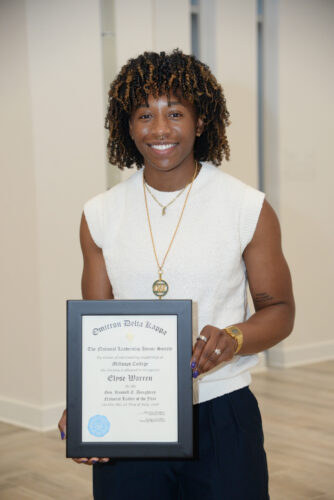 A young woman in a white, sleeveless sweater holds a black-framed certificate.